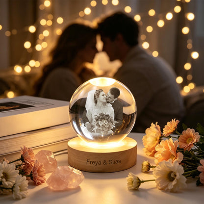 A clear glass sphere lamp featuring a laser-etched black and white photograph of a couple inside. The sphere rests on a round wooden base engraved with the text Freya & Silas, illuminated from below by a warm light.