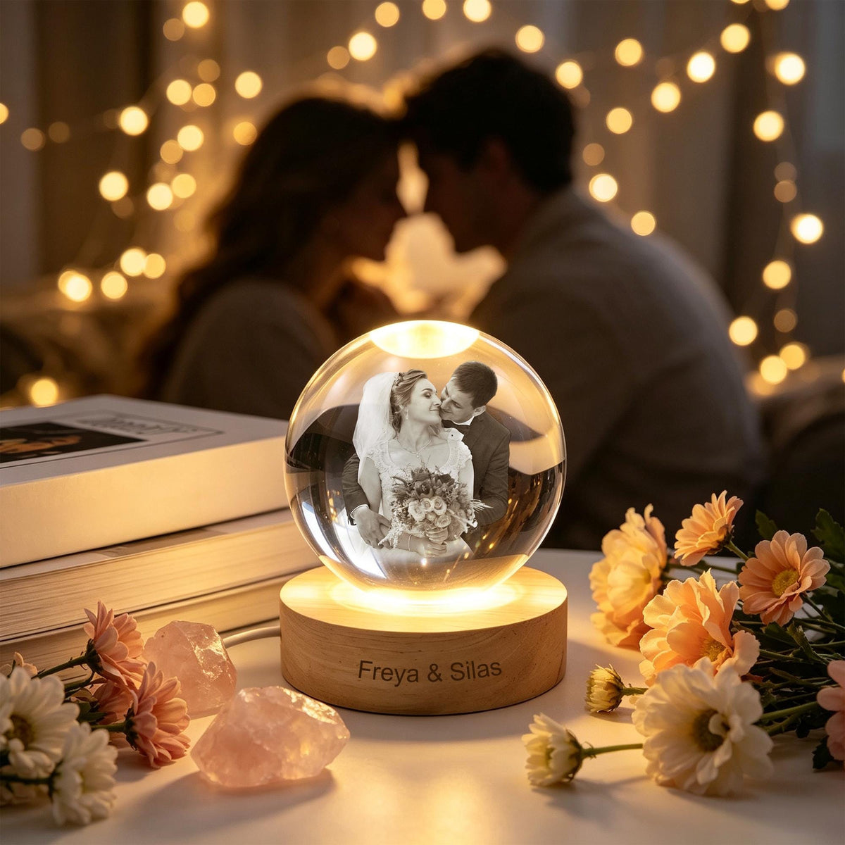 A clear glass sphere lamp featuring a laser-etched black and white photograph of a couple inside. The sphere rests on a round wooden base engraved with the text Freya & Silas, illuminated from below by a warm light.