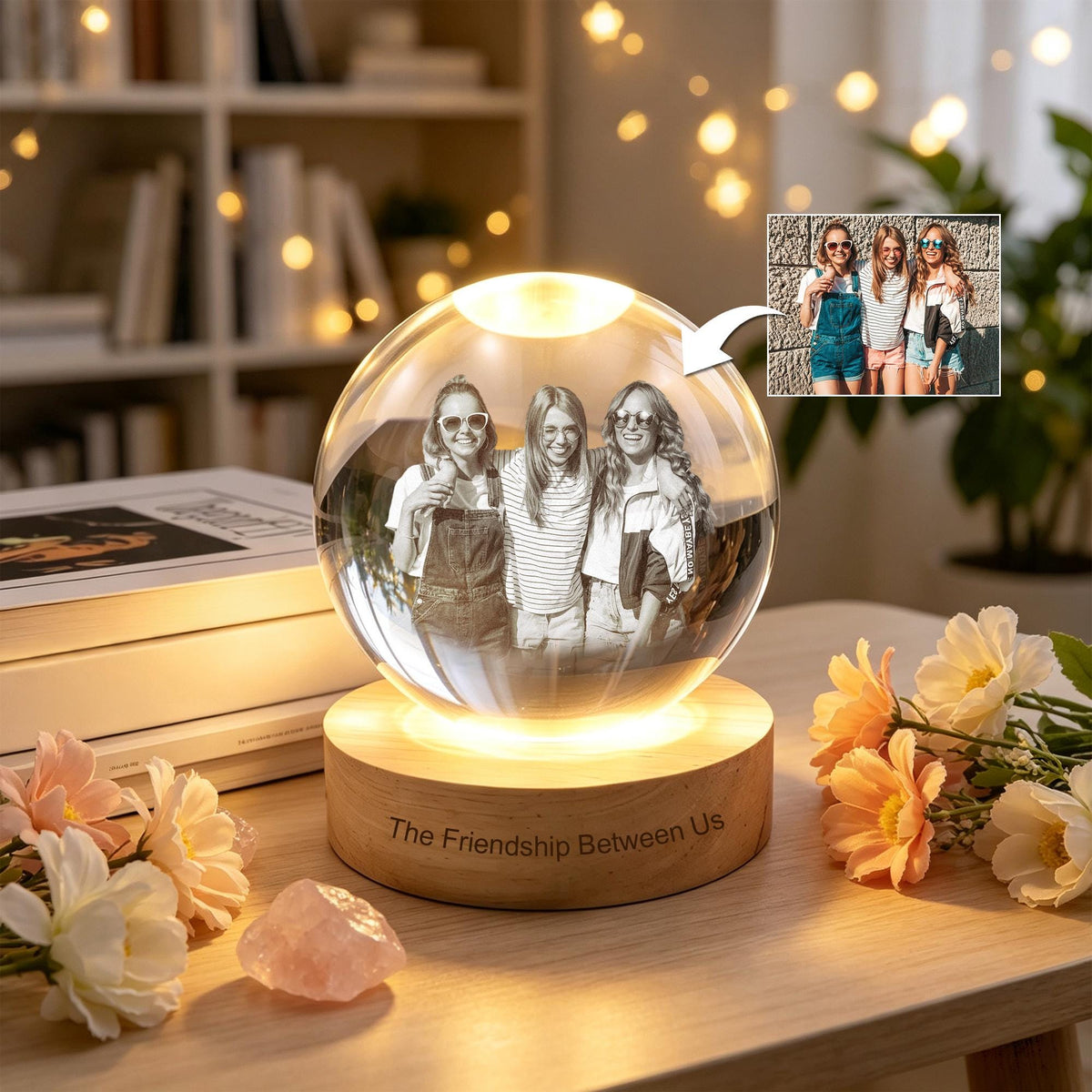 A clear glass sphere lamp featuring a laser-engraved black and white photograph of three people inside. The sphere rests on a round wooden base with the engraved text "The Friendship Between Us" on the front side of the wood.