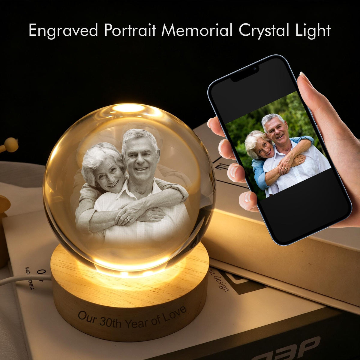 A spherical crystal light featuring an internal laser-engraved portrait of an older couple. The crystal rests on a round wooden base with the engraved text 'Our 30th Year of Love'. A smartphone displays the original photo of the couple.