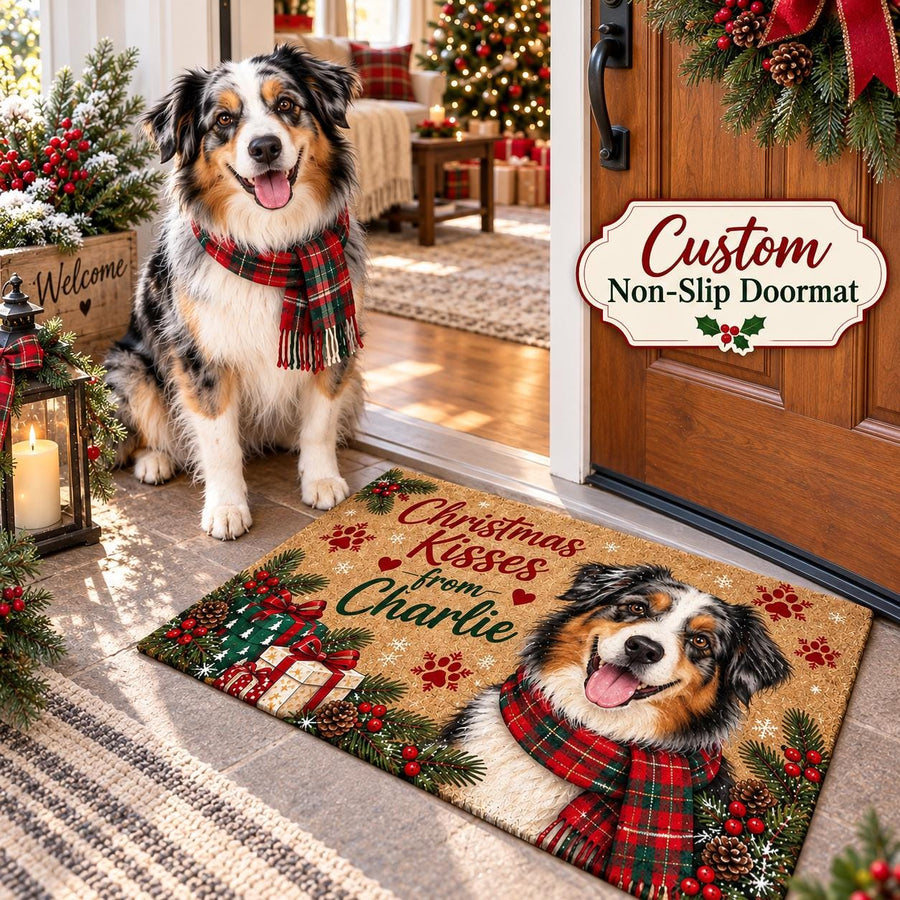 May include: A rectangular tan doormat featuring a printed illustration of an Australian Shepherd wearing a red and green plaid scarf. The mat displays the text Christmas Kisses from Charlie, surrounded by pine branches, red berries, and gift boxes.