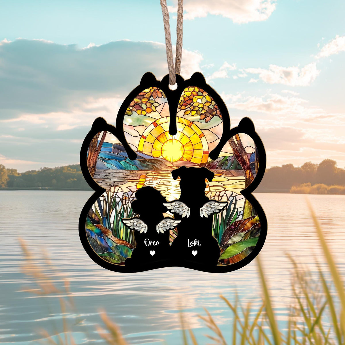 May include: A stained glass paw print ornament with a sunset scene and two dogs with angel wings. The dogs are silhouetted and the names "Oreo" and "Loki" are written below them.