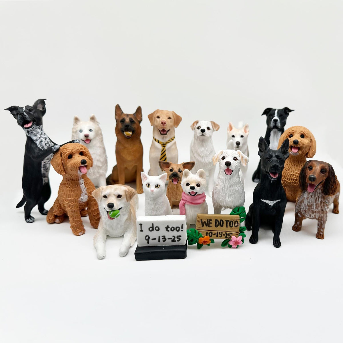 May include: A collection of dog figurines in various breeds and poses, including a black and white dog standing on its hind legs, a brown dog with a tie, and a white cat. Some figurines hold signs.