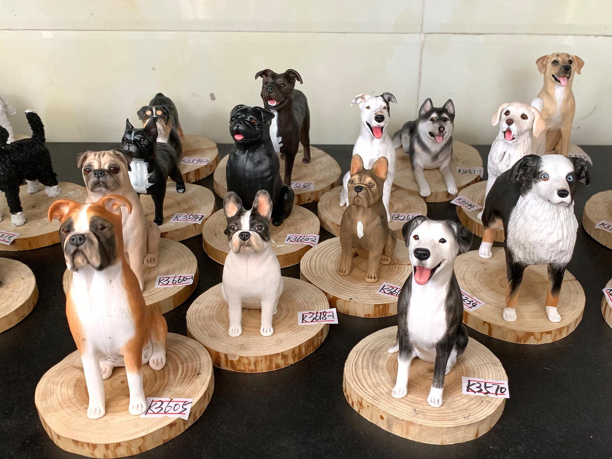 May include: A collection of dog figurines, each meticulously crafted and painted. Breeds include a Boxer, Bulldog, Pug, and Husky, among others. The figurines are displayed on wooden slices, showcasing their detailed features and varied poses.