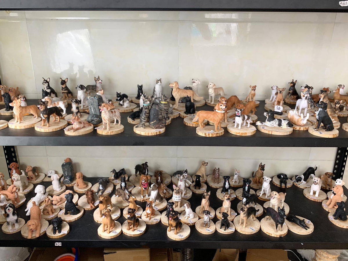 May include: A collection of dog figurines in various breeds and poses, displayed on wooden rounds. The figurines are painted in realistic colors and sit on shelves. The dogs are in different positions, such as standing, sitting, and lying down.