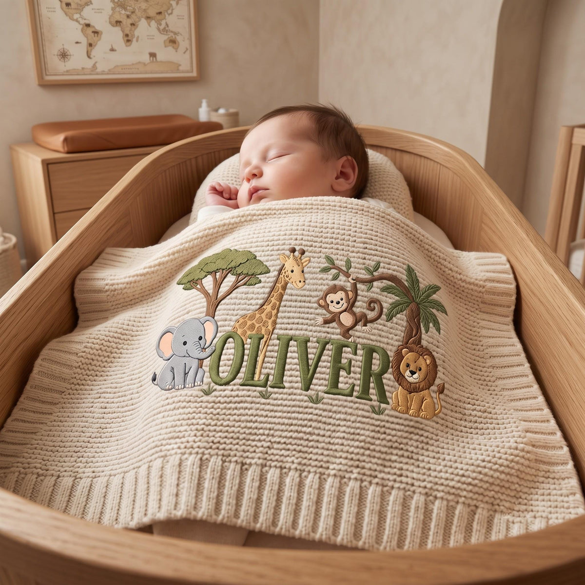 A cream-colored knit baby blanket featuring an embroidered jungle theme with a gray elephant, a yellow giraffe, a brown monkey, and a lion. The name OLIVER is stitched in large green letters across the center of the blanket.