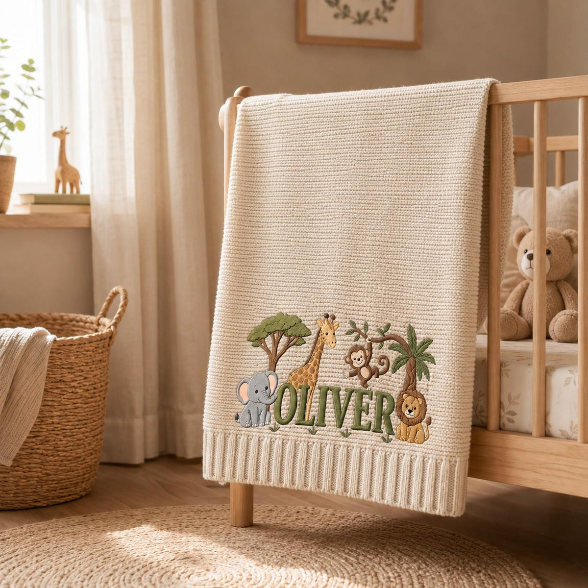 A cream-colored knit baby blanket featuring embroidered jungle animals including an elephant, giraffe, monkey, and lion. The name OLIVER is stitched in green letters across the center, surrounded by trees and foliage details.