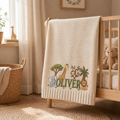 A cream-colored knit baby blanket featuring embroidered jungle animals including an elephant, giraffe, monkey, and lion. The name OLIVER is stitched in green letters across the center, surrounded by trees and foliage details.