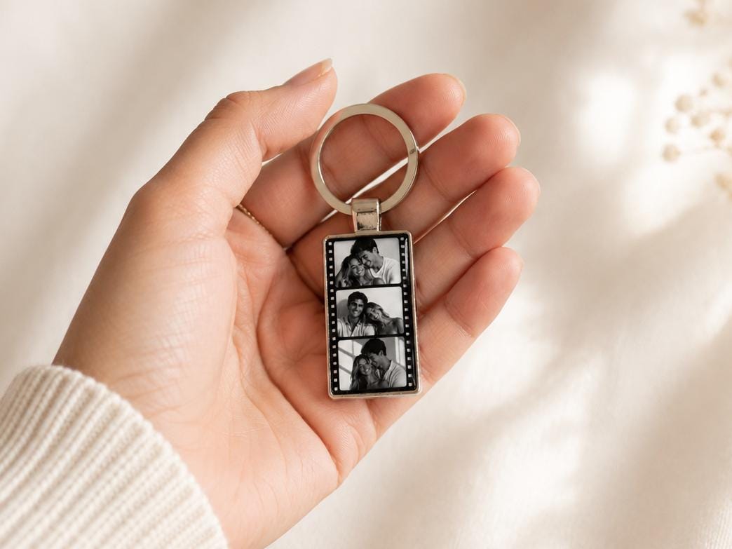 Film strip metal keychain held in hand showing size and shiny epoxy finish with 3 personalized pictures
