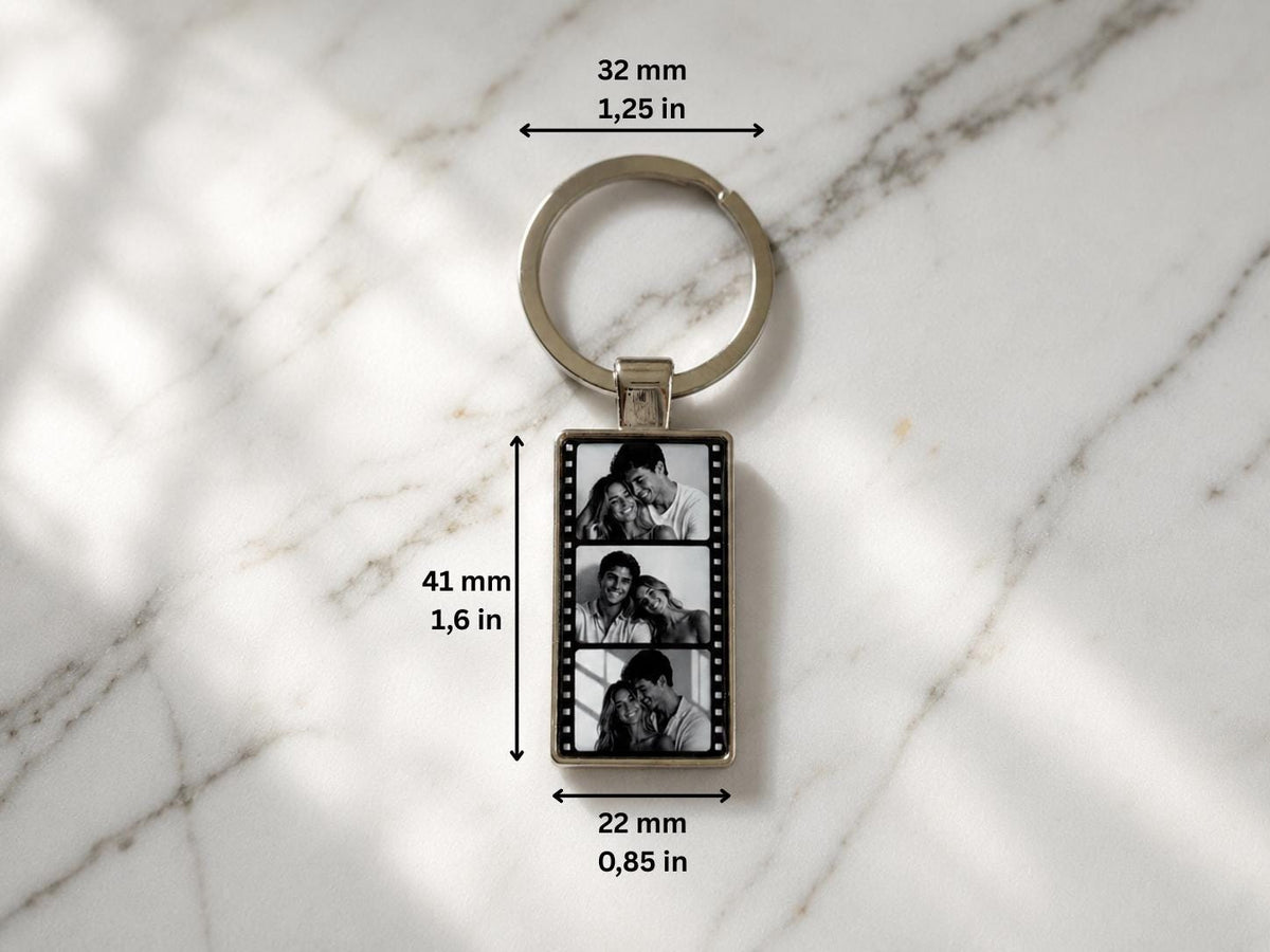 A rectangular metal keychain featuring a film strip design with three black and white photos of a couple. The keychain measures 1.6 inches in height and 0.85 inches in width, with a 1.25-inch diameter ring attached at the top.