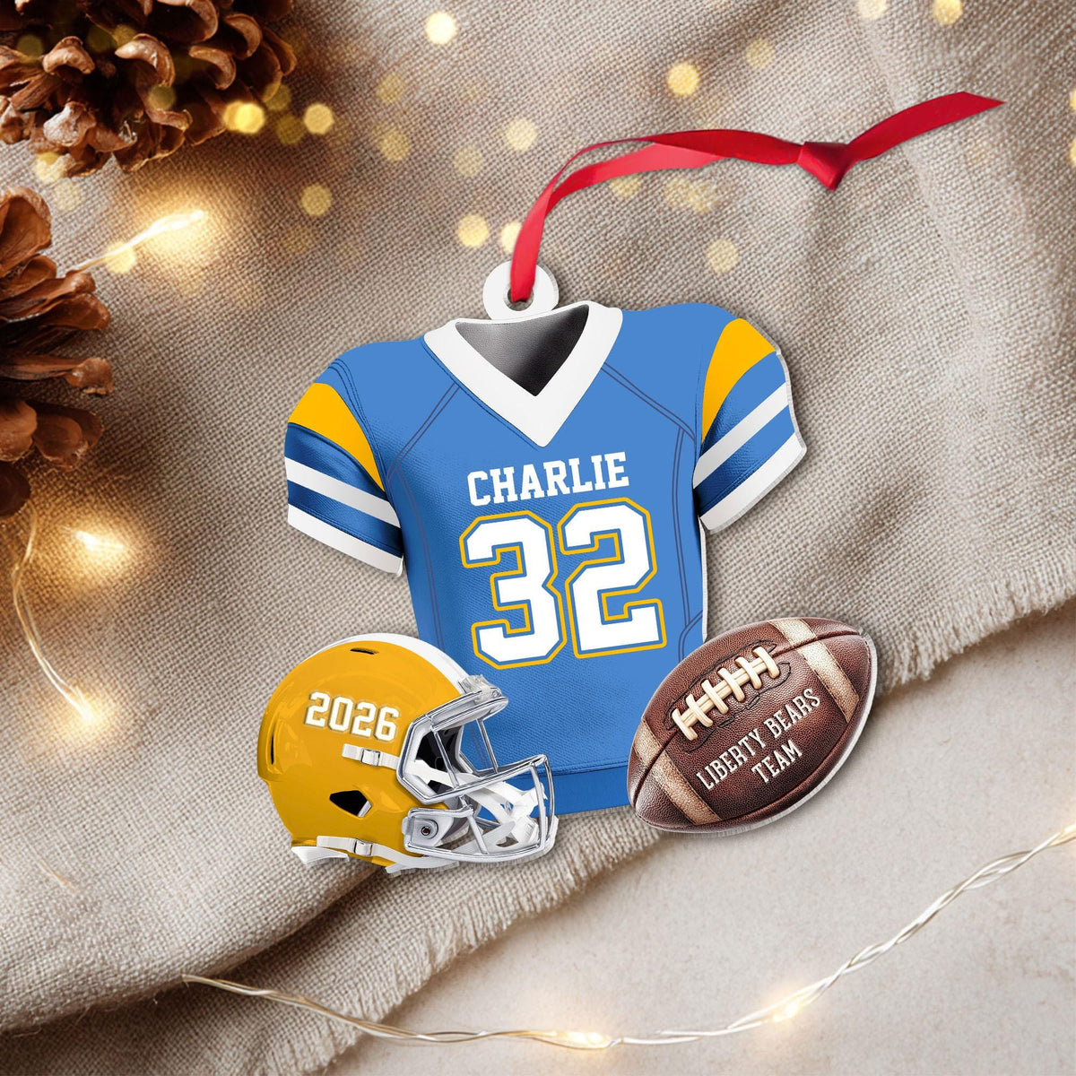 May include: A decorative ornament featuring a light blue football jersey with white and yellow accents, the name CHARLIE, and the number 32. It includes a yellow football helmet with 2026 and a brown football labeled LIBERTY BEARS TEAM.