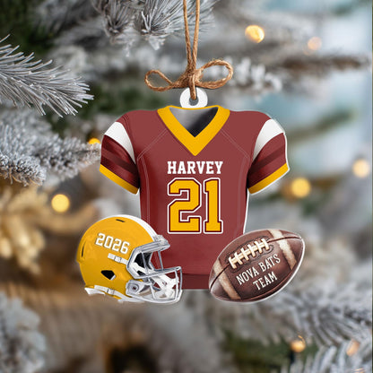May include: A maroon and yellow football jersey ornament with the name HARVEY and number 21, accompanied by a yellow helmet with 2026 and a brown football labeled NOVA BATS TEAM, all suspended by a brown twine string against a blurred background.