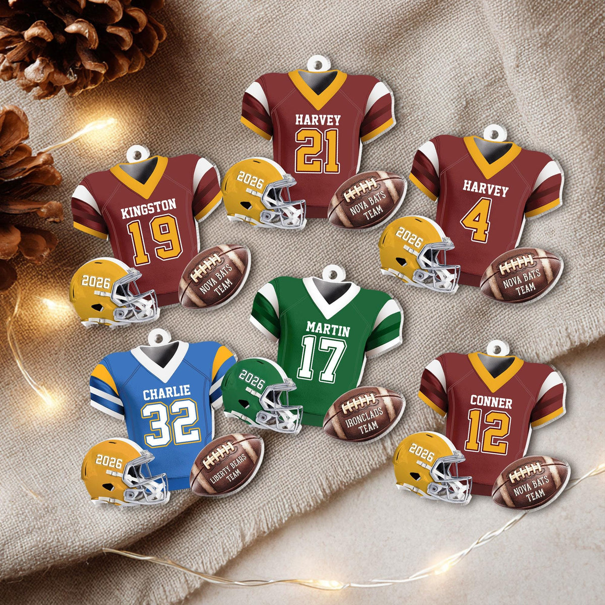 May include: A collection of flat, decorative ornaments shaped like football jerseys, helmets, and footballs. The jerseys feature names like Harvey, Kingston, Martin, Charlie, and Conner with various numbers. The footballs are labeled Nova Bats Team, Ironclads Team, or Liberty Bears Team, and the helmets are marked with the year 2026.