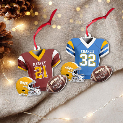 May include: Two football jersey ornaments with red ribbons, one maroon with white text HARVEY 21 and one blue with white text CHARLIE 32. Two yellow football helmets labeled 2026 and two brown footballs labeled NOVA BATS TEAM and LIBERTY BEARS TEAM.