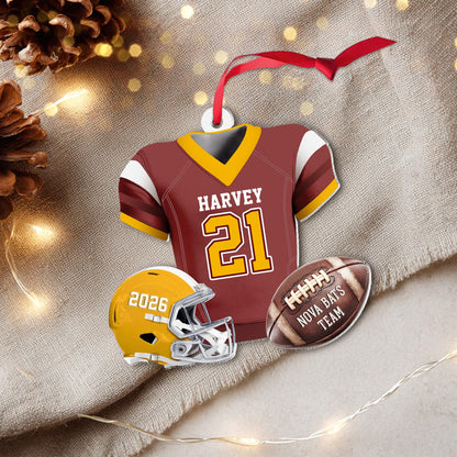May include: A maroon and gold football jersey ornament with the name HARVEY and number 21, accompanied by a yellow football helmet with the text 2026 and a brown football with the text NOVA BATS TEAM, all hanging from a red ribbon loop.
