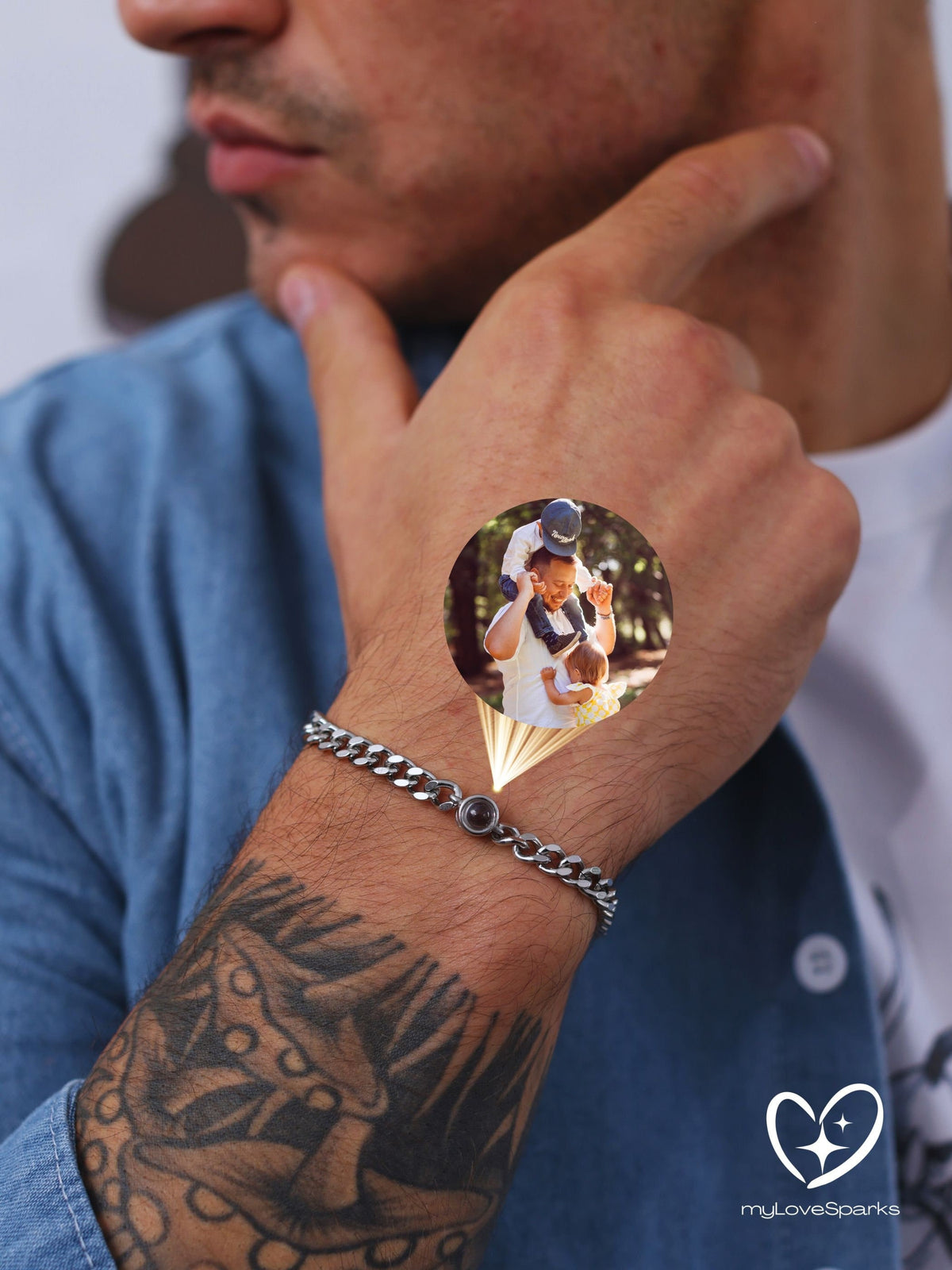 A silver curb chain bracelet with a small, round, dark red stone. The bracelet is on a person's wrist, with a tattoo visible on the forearm. A small circular image is superimposed on the wrist.