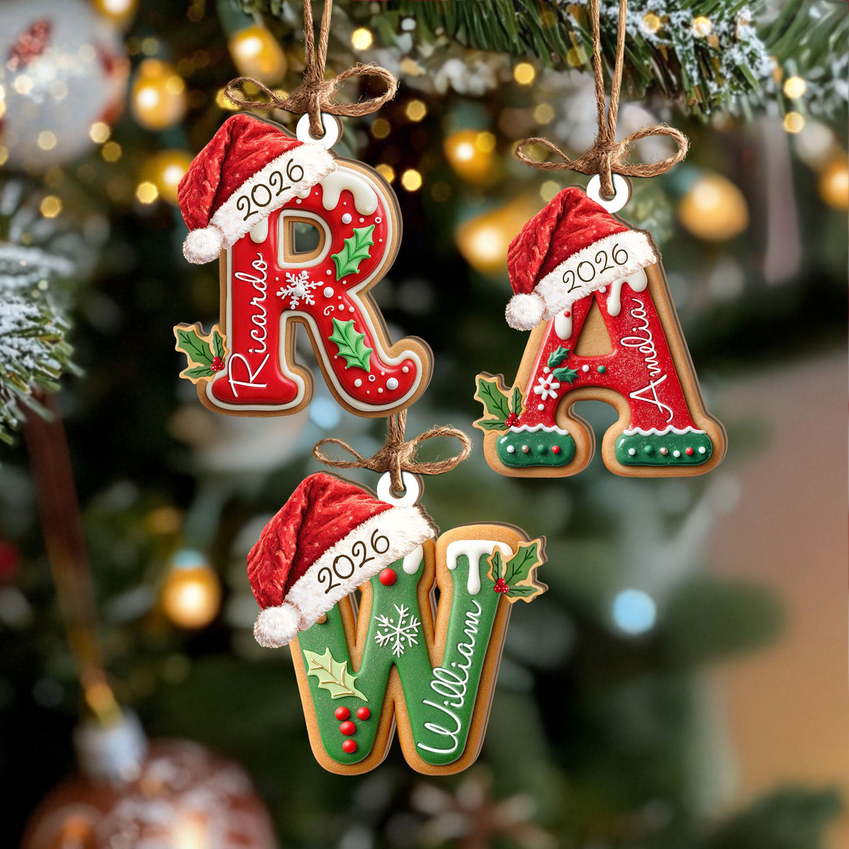 May include: Three letter-shaped Christmas ornaments shaped like gingerbread cookies. The letters R, A, and W are decorated with white icing, holly leaves, and red berries. Each letter wears a red Santa hat with the year 2026 and a name printed on it.
