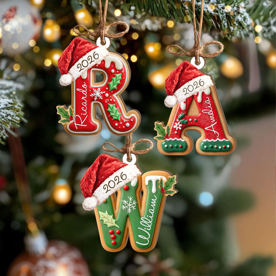 May include: Three letter-shaped Christmas ornaments shaped like gingerbread cookies. The letters R, A, and W are decorated with white icing, holly leaves, and red berries. Each letter wears a red Santa hat with the year 2026 and a name printed on it.