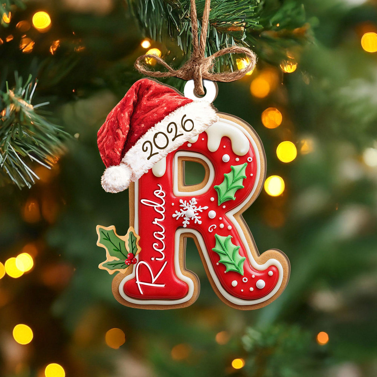May include: A letter R Christmas ornament shaped like a gingerbread cookie with red icing, white trim, and green holly leaves. It features a red Santa hat with the year 2026 and the name Ricardo written in white script, hanging by a brown twine loop.