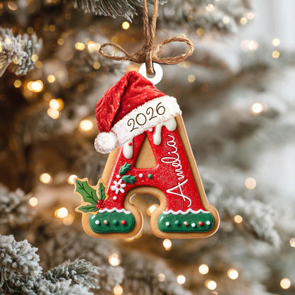 May include: A gingerbread-style letter A Christmas ornament featuring a red Santa hat with the year 2026 printed on the white trim. The letter is decorated with red and green icing, white holly accents, and the name Amelia written in white script.