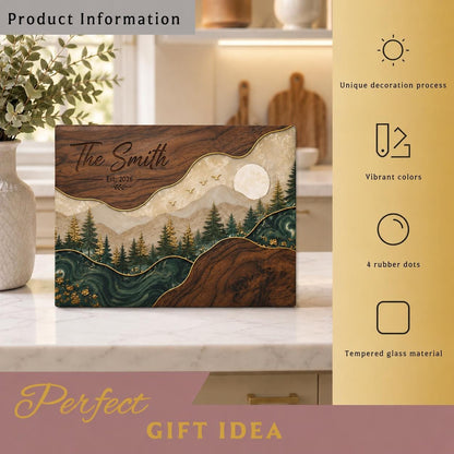A rectangular tempered glass cutting board featuring a dark wood grain pattern on the top and bottom edges, with a central landscape illustration of a forest, mountains, a full moon, and the text The Smith Est. 2026.