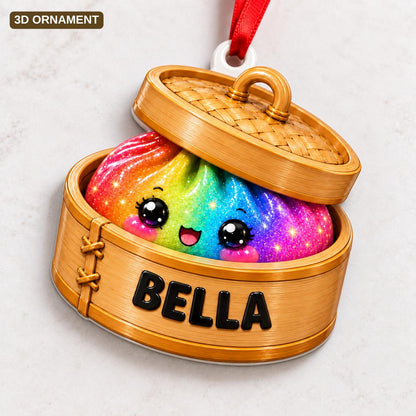 A 3D ornament shaped like a bamboo steamer basket containing a rainbow-colored, glittery dumpling with a smiling face. The side of the wooden-textured steamer is printed with the name BELLA in bold black capital letters.