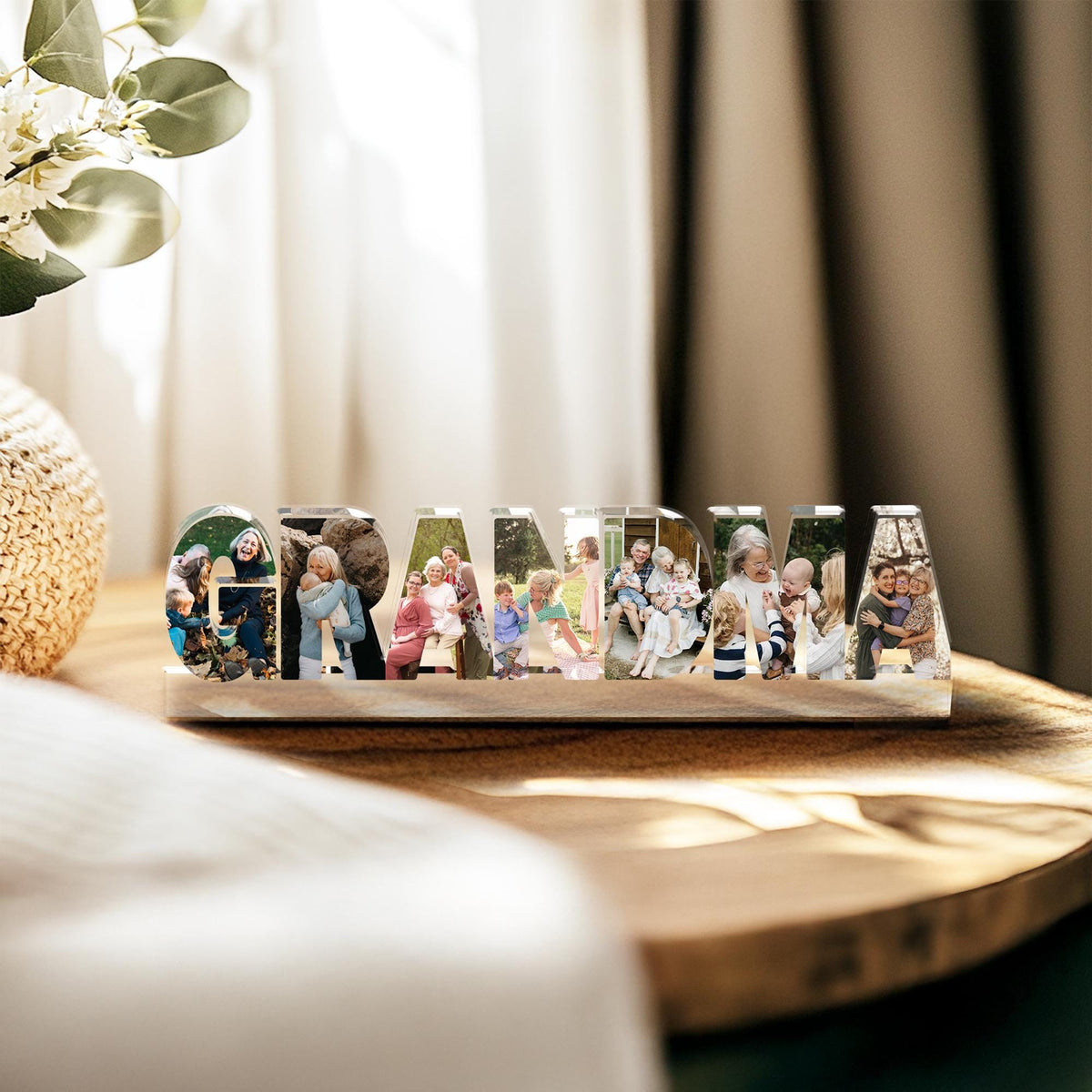 May include: A wooden block with the word "GRANDMA" spelled out in clear acrylic letters. Each letter contains a different family photo. The block sits on a wooden surface, with a blurred background.