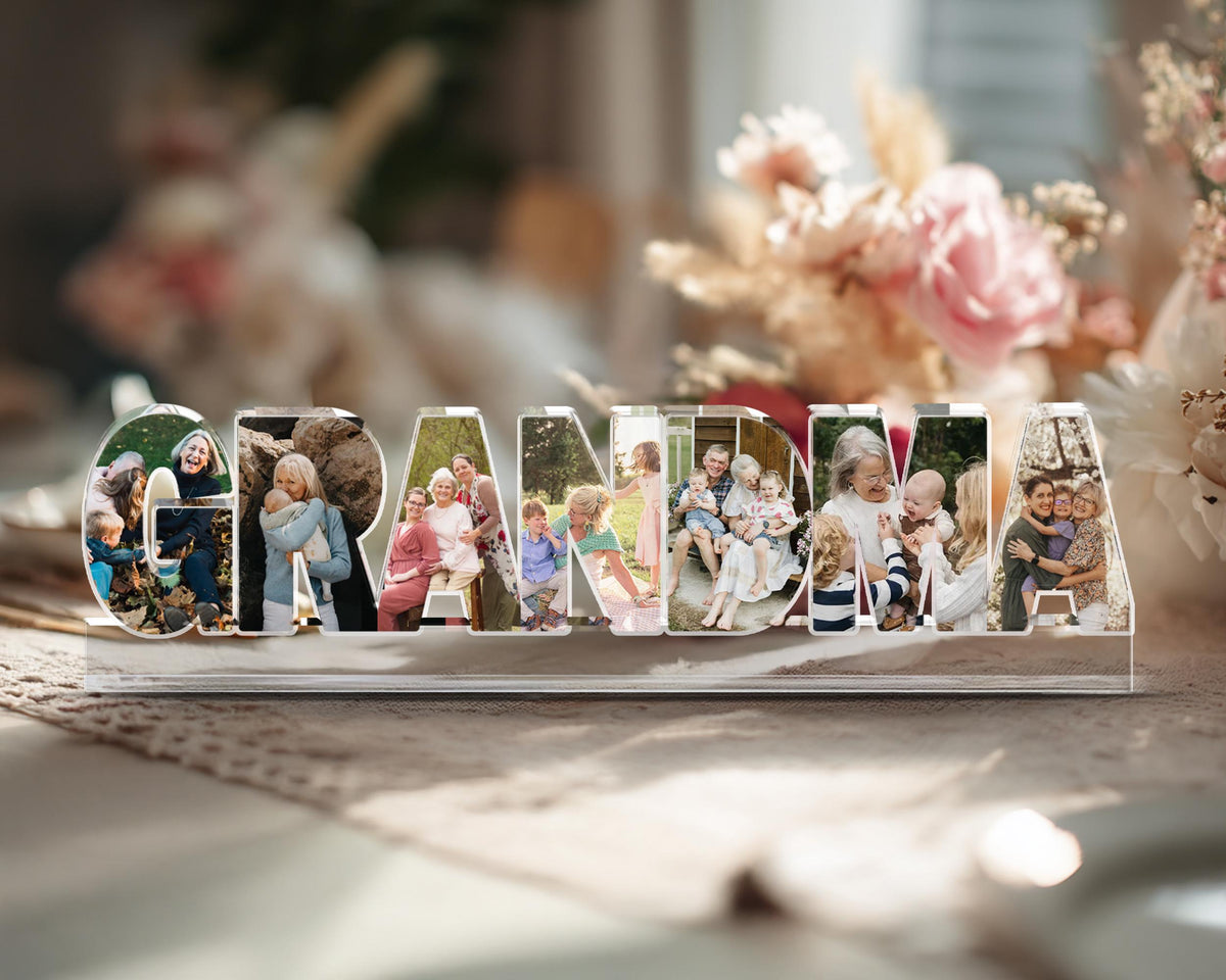 May include: A clear acrylic photo display spelling out the word "GRANDMA". Each letter holds a different family photo. The display sits on a table with a blurred floral background, making it a personalized gift.