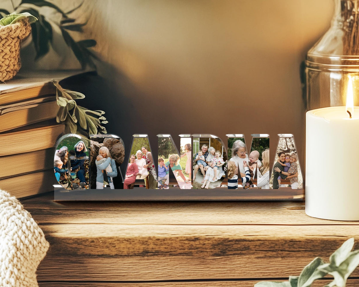 May include: A decorative wooden sign spelling "GRANDMA" with individual letters holding family photos. The sign is displayed on a wooden surface, with a lit candle and books in the background. A thoughtful gift.