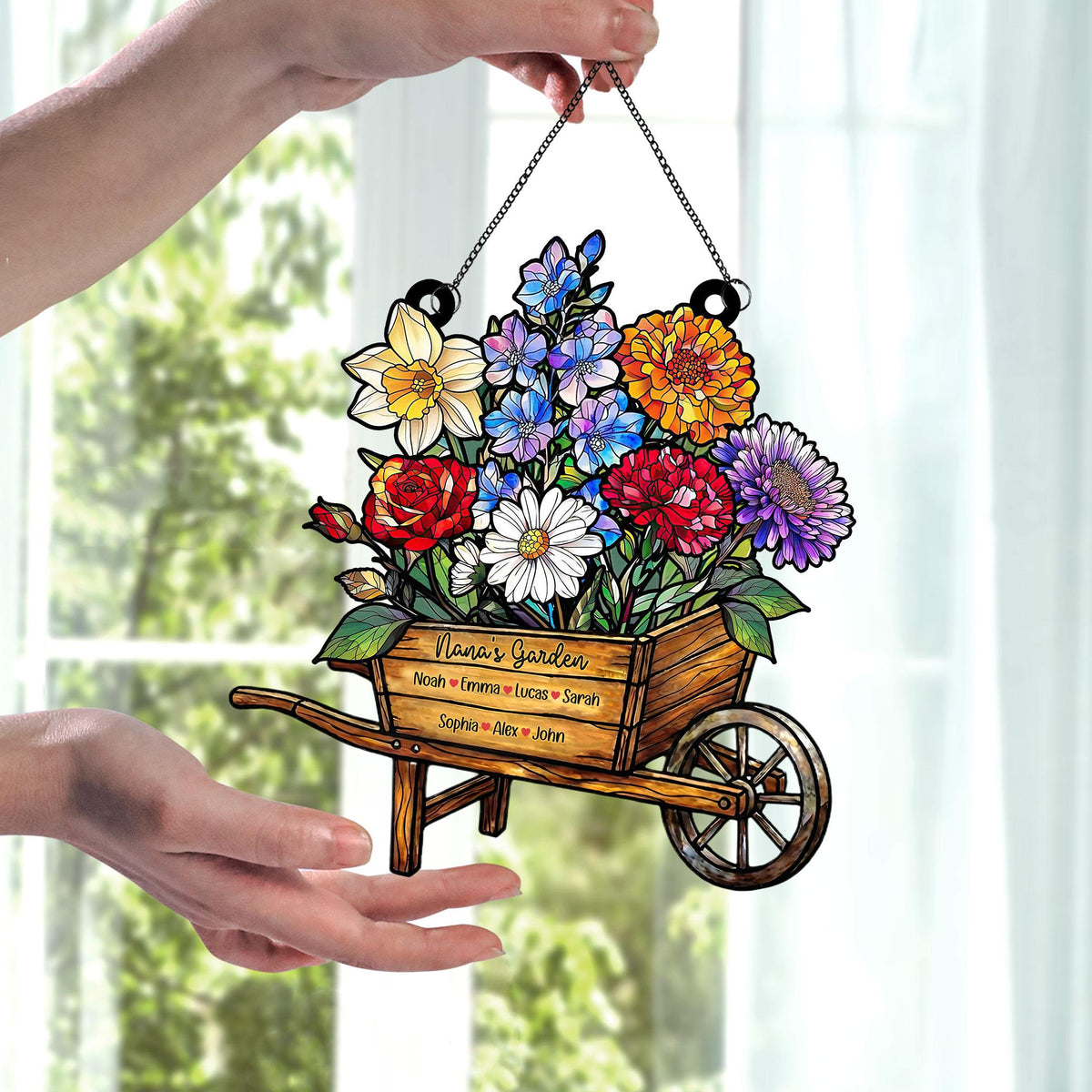 May include: A decorative garden-themed hanging sign featuring a wooden wheelbarrow overflowing with colorful flowers. The sign includes the text "Nana's Garden" and several names. The sign is suspended by a chain.