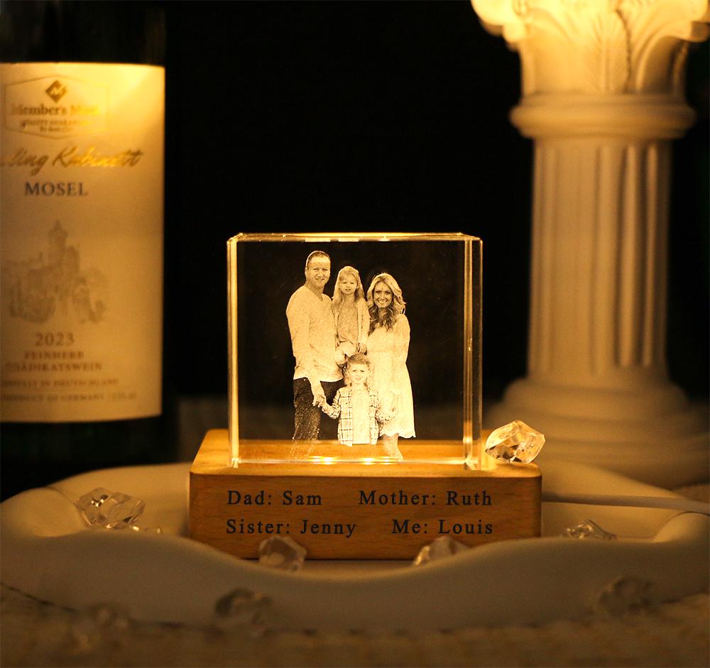A clear rectangular glass block featuring a laser-etched family portrait, illuminated from below by a wooden base. The base is engraved with the text: Dad: Sam, Mother: Ruth, Sister: Jenny, Me: Louis, creating a personalized display piece.
