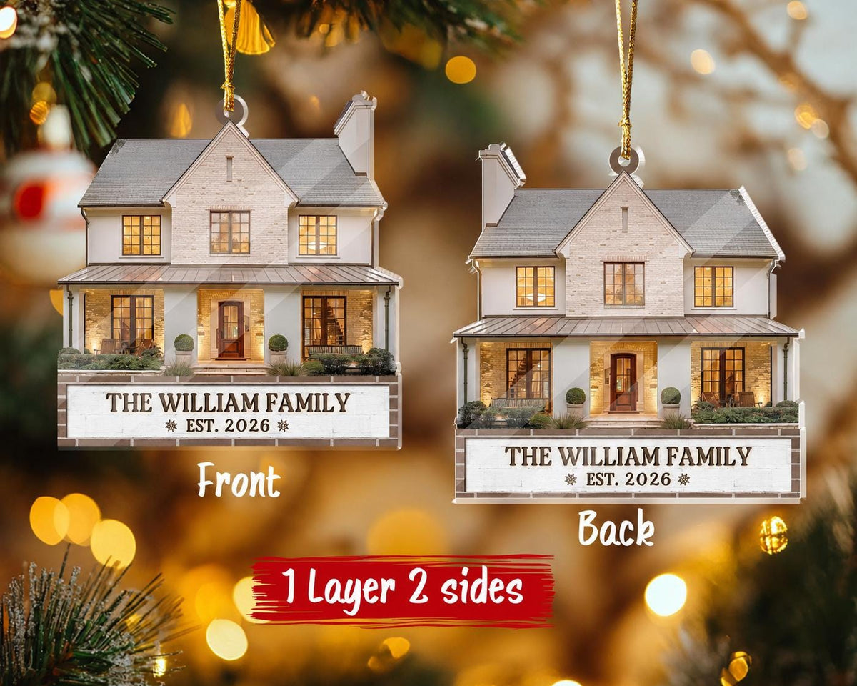 May include: A two-sided house-shaped Christmas ornament featuring a printed image of a two-story home with a white brick facade and a dark roof. The base includes the text THE WILLIAM FAMILY EST. 2026. A gold string is attached for hanging.