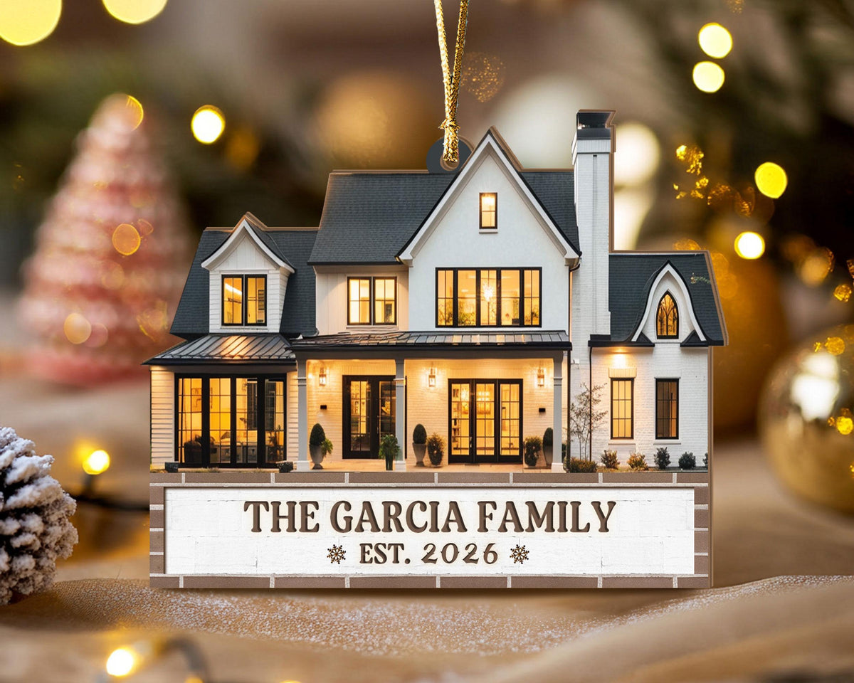 May include: A flat, house-shaped Christmas ornament featuring a white two-story home with a dark gray roof, black window frames, and a chimney. The base displays the text THE GARCIA FAMILY and EST. 2026 with small snowflake icons on each side.