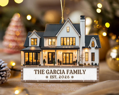 May include: A flat, house-shaped Christmas ornament featuring a white two-story home with a dark gray roof, black window frames, and a chimney. The base displays the text THE GARCIA FAMILY and EST. 2026 with small snowflake icons on each side.