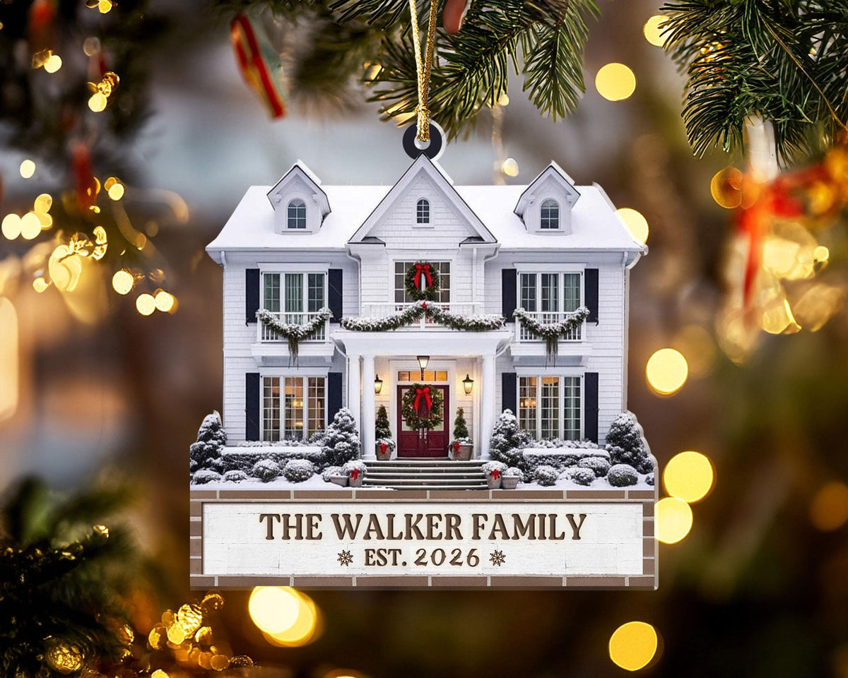 May include: A flat, two-dimensional Christmas tree ornament shaped like a white two-story house with snow on the roof, green garlands, and red wreaths. A rectangular base features the text THE WALKER FAMILY and EST. 2026 with a gold hanging cord.