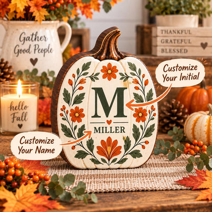 May include: A decorative wooden pumpkin cutout featuring a cream-colored front with a dark green letter M, the name MILLER, and orange floral illustrations. Two orange arrows point to the text with labels reading Customize Your Initial and Name.