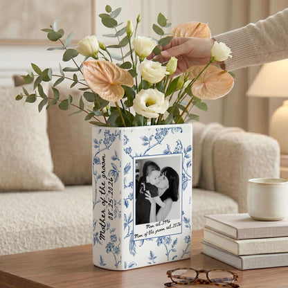 A rectangular white ceramic vase featuring a blue floral pattern. The front displays a black and white photograph of two people with the text 'Mom est. 1996' and 'Mom of the groom est. 2026'. The side includes the text 'Mother of the groom 08.25.2026'.