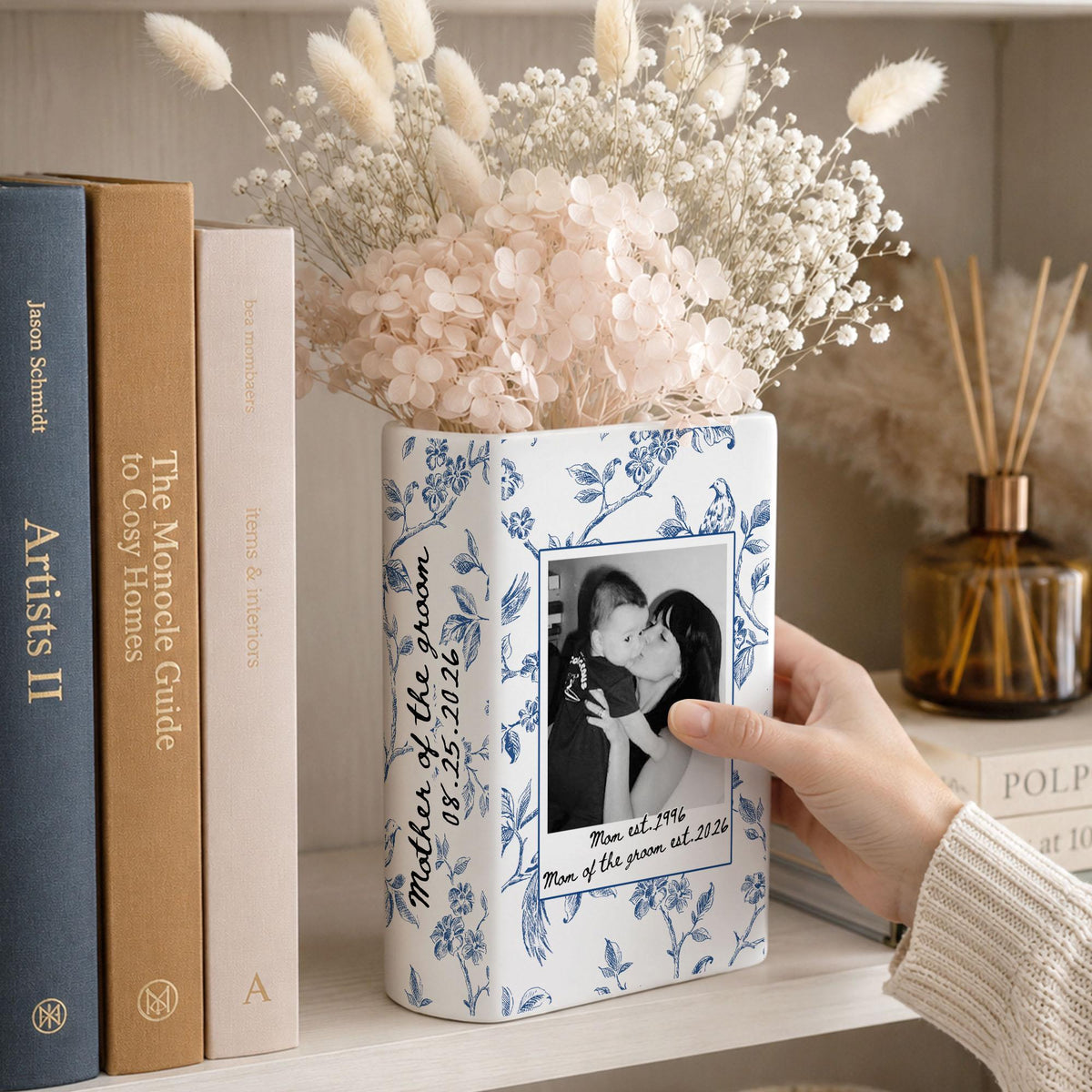 A rectangular white ceramic vase with a blue floral pattern, featuring a black and white photograph of a person holding a child. The text reads Mother of the groom 08.25.2026 and Mom est. 1996 Mom of the groom est. 2026 on the front surface.