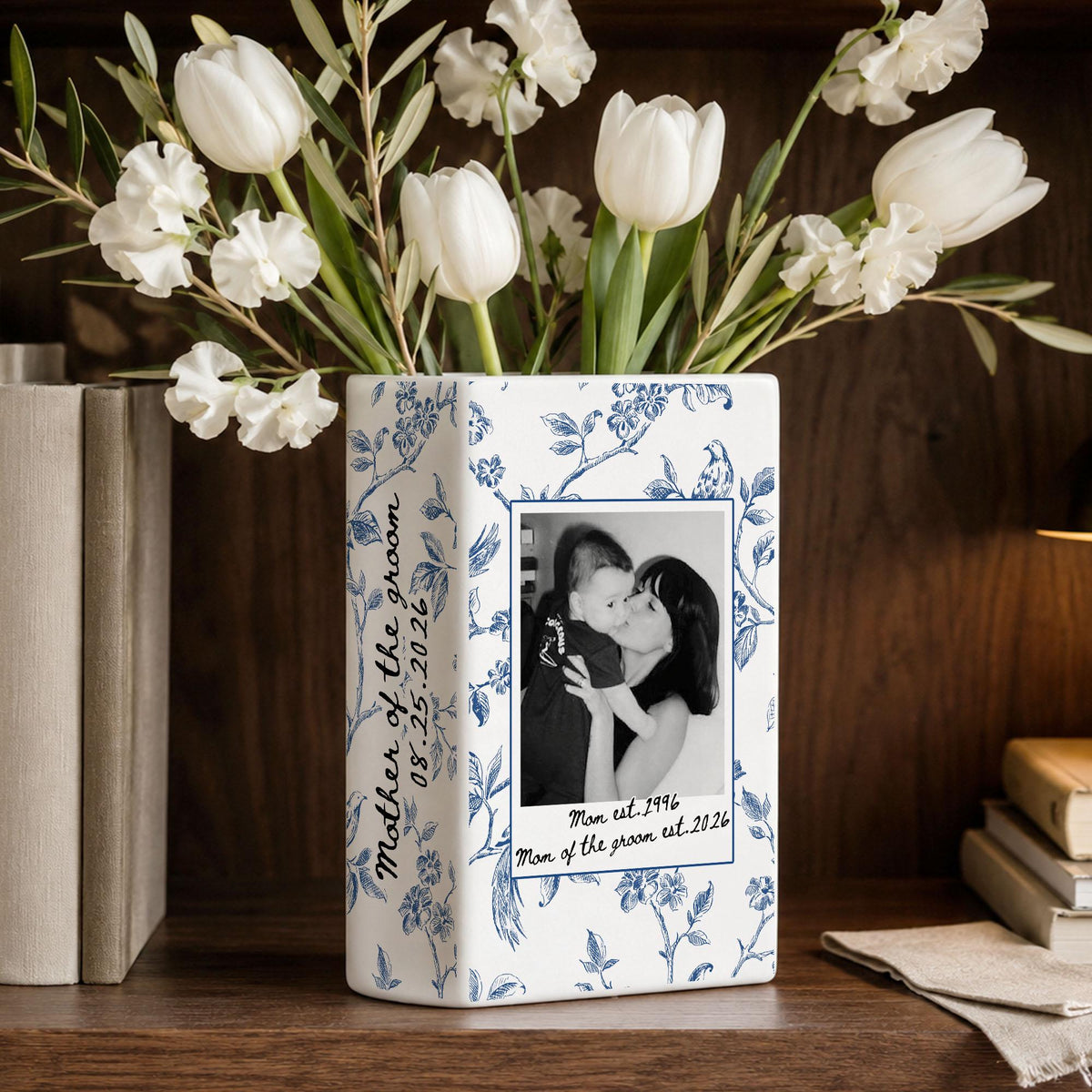 A rectangular white ceramic vase featuring a blue floral pattern. The front displays a black and white photograph of a person holding a child, with the text "Mom est. 1996" and "Mom of the groom est. 2026" printed below the image.