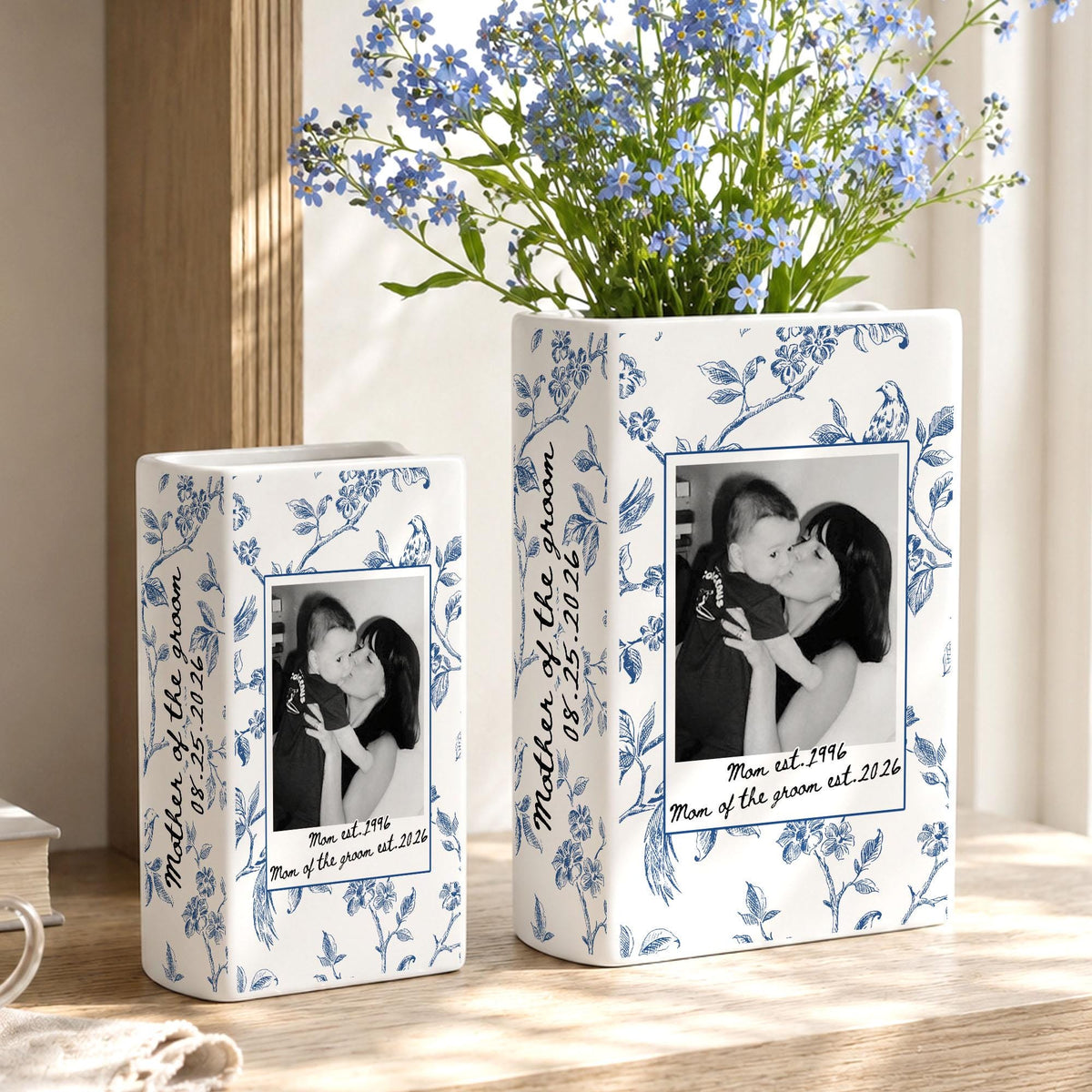 Two rectangular white ceramic vases decorated with blue floral patterns. Each vase features a black and white photograph of a person holding a child, with the text "Mother of the groom 08.25.2026" and "Mom est. 1996 Mom of the groom est. 2026".