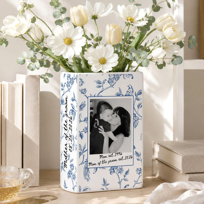 A rectangular white ceramic vase featuring a blue floral pattern and a central black and white photograph of a person holding a child. The text "Mother of the groom 08.25.2026" and "Mom est. 1996 Mom of the groom est. 2026" is printed on the surface.