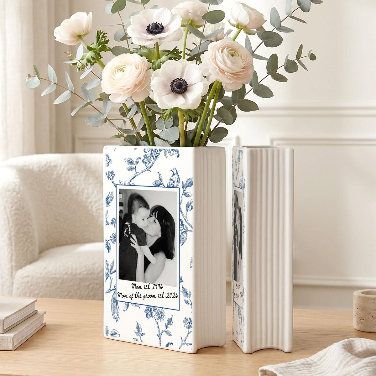 A rectangular white ceramic vase featuring a blue floral toile pattern and a central black and white photograph of a person holding a child. The text below the photo reads "Mom est. 1996" and "Mom of the groom est. 2026".