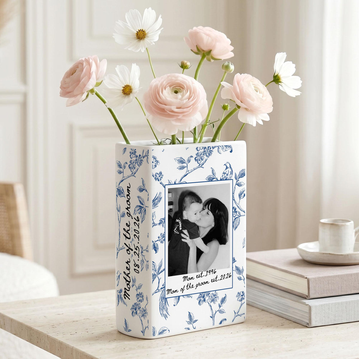 A rectangular white ceramic vase featuring a blue floral pattern, a black and white photograph of a person holding a child, and the text "Mother of the groom 08.25.2026" and "Mom est. 1996 Man of the groom est. 2026" filled with pink and white flowers.