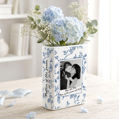 A rectangular white ceramic vase featuring a blue floral pattern, a black and white photograph of two people, and the text "Mother of the groom 08.25.2026" and "Mom est. 1996 Mom of the groom est. 2026" filled with light blue hydrangea flowers.