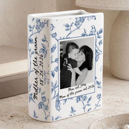 A white ceramic rectangular vase featuring a blue floral pattern. The front displays a black and white photograph of a person holding a child, with the text "Mother of the groom 08.25.2026" and "Mom est. 1996 Mom of the groom est. 2026" printed on it.