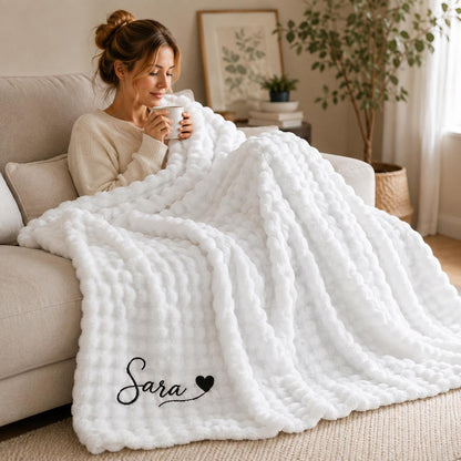 A plush white textured throw blanket featuring a repeating bubble pattern. The bottom corner of the blanket is embroidered with the name Sara in a black cursive script, followed by a small solid black heart icon.