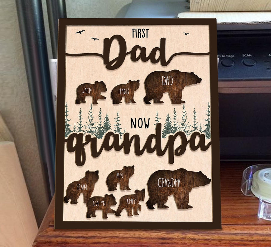 May include: A wooden sign with a brown background and a cutout design of bears. The sign reads "First Dad Now Grandpa" with the names of the children and grandchildren listed below the bears.