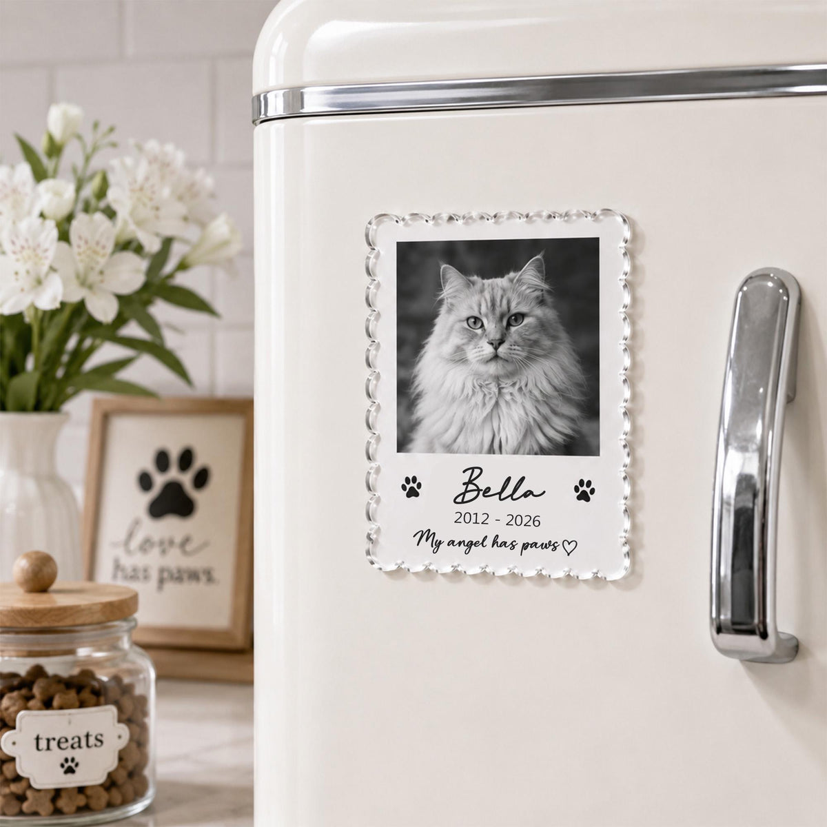 May include: A rectangular acrylic magnet with a scalloped edge featuring a black and white photograph of a cat. The text reads Bella, 2012-2026, and My angel has paws, accompanied by two small paw print icons and a heart symbol.