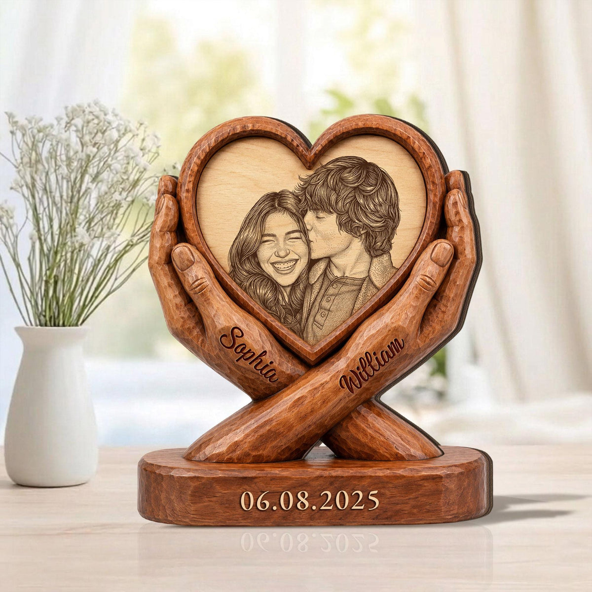A wooden heart-shaped photo frame with a carved image of a couple. The frame is held by carved wooden hands. The names "Sophia" and "William" are carved on the hands. The date "06.08.2025" is carved on the base.