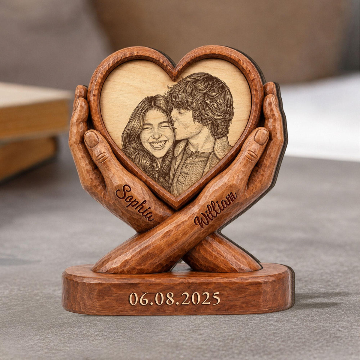 A wooden heart-shaped photo frame with a carved image of a couple kissing. The frame is held by carved wooden hands. The names "Sophia" and "William" are inscribed on the hands. The date "06.08.2025" is carved on the base.